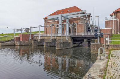 Am Ende eines Gewässers steht ein Klinkergebäude, daneben eine Hubbrücke. Das Gewässer fließt unter dem Gebäude durch.