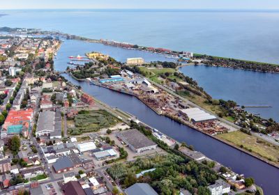 Luftbild des Handelshafen im Vordergrund. Rechts davon Ausläufer des Banter See, im Hintergrund das offene Meer.