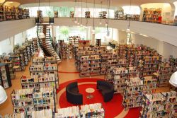 Blick von der umlaufenden Empore in den Saal der Bibliothek. Zwischen den Bücherregalen steht in der Saalmitte ein kleiner Tisch, der von zwei halbkreisförmigen Sofas umgeben ist.