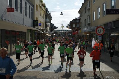 An einem sonnigen Vormittag bewegen sich die Teilnehmerinnen und Teilnehmer des Gorch-Fock-Marathons in der Marktstraße direkt auf die Kamera zu. Das Läuferfeld reicht vom Vordergrund in Höhe der Grenzstraße bis hin zur Virchowstraße. An ihrer Laufkleidung haben die Läufer Zettel mit ihren Startnummern befestigt.