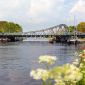 Deichbrücke an einem sommerlichen Tag. Aufgenommen aus Richtung des Großen Hafens über die Blüten der Pflanzen an der Uferböschung.